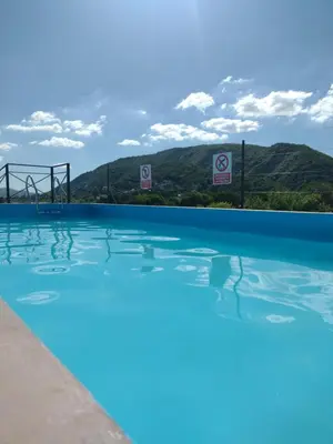 a swimming pool with blue water and mountains in the background at Dpto en alquiler temporario en VCPaz in Villa Carlos Paz