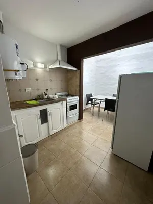 a kitchen with white cabinets and a table and a refrigerator at AMPLIOS Departamentos PASAJE TUCUMÁN in Alta Gracia