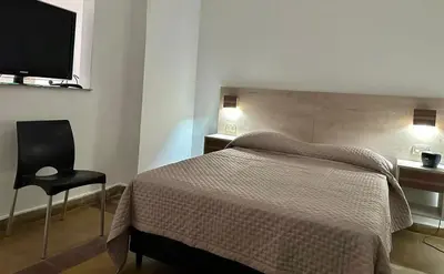a bedroom with a bed and a chair and a television at AMPLIOS Departamentos PASAJE TUCUMÁN in Alta Gracia