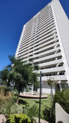 a tall white building with a palm tree in front of it at Departamento con seguridad 24hs, gym y pileta! in Cordoba