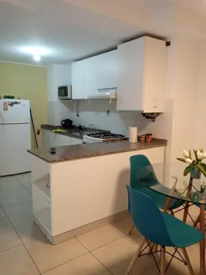 a kitchen with white cabinets and a green chair at Departamentos NG CENTRO Carlos Paz in Villa Carlos Paz