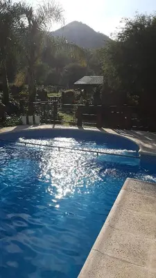 a blue swimming pool with a bench and palm trees at Cabañas Ranger in Santa Rosa de Calamuchita