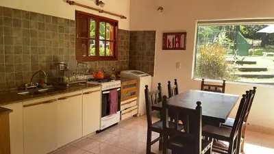 a kitchen with a table and a sink and a table and chairs at Casa con jardín, pileta, asador, y vistas al lago en Embalsina in Villa del Dique