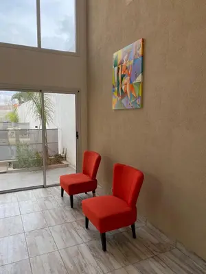 a waiting room with two red chairs and a painting at Cañas Suites Villa Cura Brochero in Villa Cura Brochero