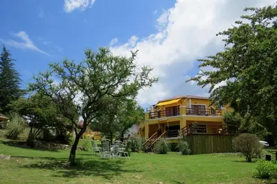 a yellow house with tables and chairs in the yard at LAS PRINCESAS Cabañas frente al rio in Los Reartes