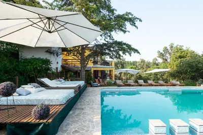 a swimming pool with two beds and an umbrella at LAS PRINCESAS Cabañas frente al rio in Los Reartes