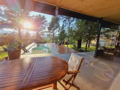 a wooden table and chair on a deck with a pool at Colores de Manantiales in Villa General Belgrano