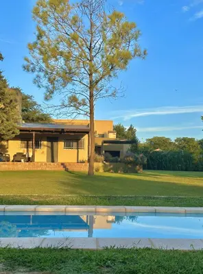 a tree in front of a house with a swimming pool at Cabaña Sierras Chicas in Villa Anizacate
