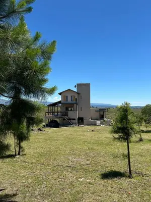 a house in the middle of a field with trees at Cabañas Casa Flor Yacanto in Villa Yacanto