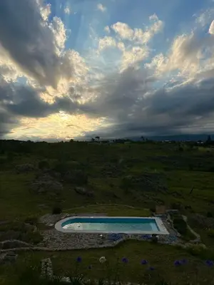 a swimming pool in a field with a cloudy sky at Cabañas Casa Flor Yacanto in Villa Yacanto