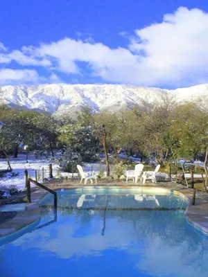 a swimming pool with two white chairs and a snow covered mountain at Cabañas en Piedras Maia in Merlo