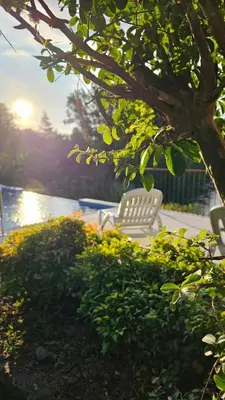a white chair sitting under a tree next to the water at El Potrerillo Posada in Santa Rosa de Calamuchita