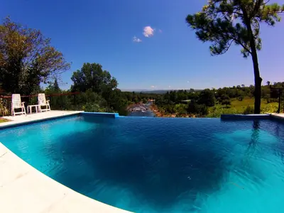 a swimming pool with two chairs and a view of a river at El Potrerillo Posada in Santa Rosa de Calamuchita