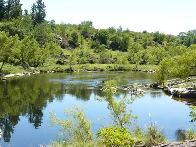a river with blue water and trees in the background at El Potrerillo Posada in Santa Rosa de Calamuchita