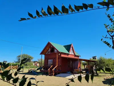 a small wooden house with a playground in a field at Cabaña en Los Reartes in Villa General Belgrano