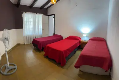 a room with two beds with red sheets and a fan at Casa zona CUCÚ de 2 dormitorios in Villa Carlos Paz