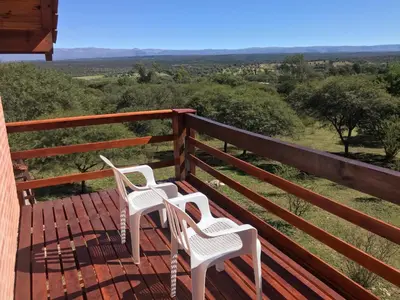 two white chairs sitting on a deck with a view at Cabaña EL GALLO in Villa General Belgrano