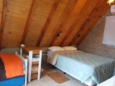 a room with two beds and a table in a attic at La Estacion in Santa Rosa de Calamuchita
