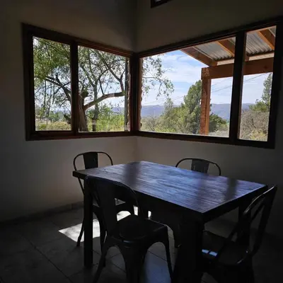 a table and chairs in a room with windows at Las Casitas de Piedra II in Villa General Belgrano