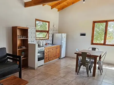a kitchen with a table and a refrigerator and a table and chairs at Las Casitas de Piedra II in Villa General Belgrano
