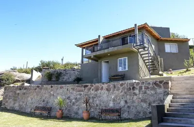 a house with a stone wall and two chairs at Complejo Lamarca in Villa Carlos Paz