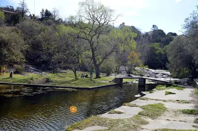 a river with a bridge and people sitting on the grass at Villa Somena in Tanti