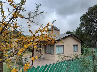 a house behind a fence with a tree at Chalet El Buho in Villa General Belgrano