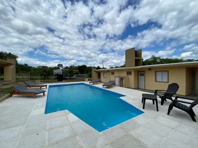 a swimming pool with chairs and a house at Cabañas Emilia in Mina Clavero