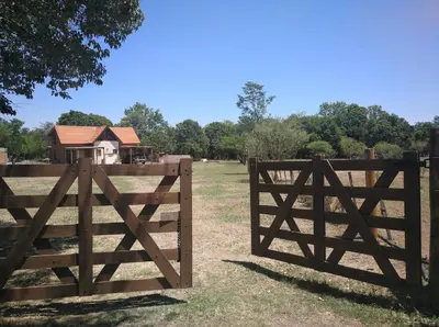 a wooden gate in a field with a house behind it at Cabañas el Ñato in Nono