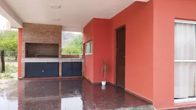 a house with a red wall and a potted plant at Cabañas Nakupenda in Villa Carlos Paz