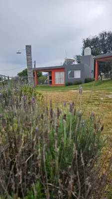 a house sitting on top of a field with flowers at Cabañas Nakupenda in Villa Carlos Paz