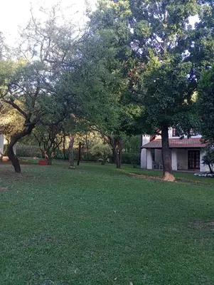 a field of green grass with trees and a house at Loma Dorada Cabañas in Villa General Belgrano