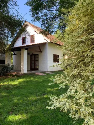 a white house with a grass yard and trees at Loma Dorada Cabañas in Villa General Belgrano