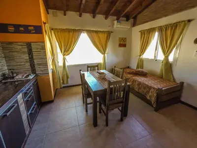 a kitchen and dining room with a table and a bed at Cabañas & Suites Vista Hermosa in Los Reartes