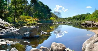 a river with rocks and trees and clouds in the water at Chalet y Cabaña de montaña Esmeralda in Villa del Dique
