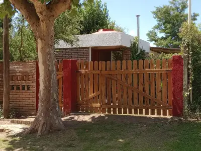 a wooden fence in front of a house with a tree at CASITA PINTORESCA EN LAS SIERRAS Y LAGO in San Roque