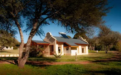 a small white house with a tree in the foreground at Cabañas Sierra Serena in Villa General Belgrano