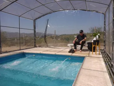 a man sitting on a chair next to a swimming pool at Complejo El Bonsai in Villa Santa Cruz del Lago