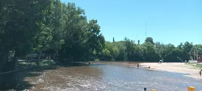 a river next to a beach with people on it at ARROYO SERRANO-MINA CLAVERO in Mina Clavero