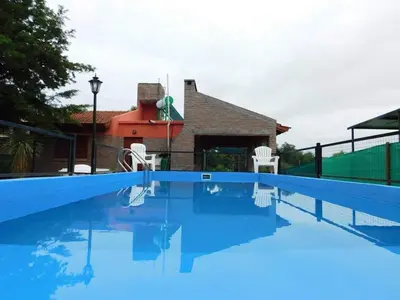 a swimming pool with two white chairs and a house at Dúplex PIRULO in Villa Cura Brochero