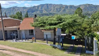 a house with a fence and mountains in the background at Casa con piscina vista al lago montañas-Sierras de Córdoba in Villa Parque Siquiman
