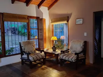 a living room with two chairs and a table and windows at Casa en Sierras de Córdoba, Villa la Bolsa. in La Bolsa