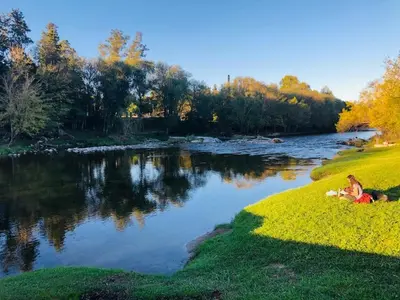 two people sitting on the grass next to a river at Casa en Sierras de Córdoba, Villa la Bolsa. in La Bolsa