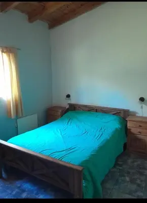 a bedroom with a wooden bed with a green blanket at Cabaña Serrana in Santa Rosa de Calamuchita