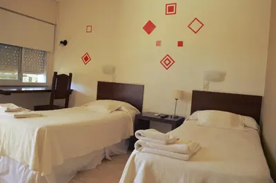 two beds in a room with red squares on the wall at Hotel La Posada del Viajero in Río Cuarto