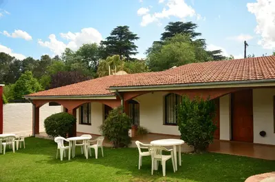 a house with white chairs and tables in the yard at Apart Cabañas La Estancia in Mina Clavero