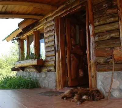 a dog laying in front of a wooden house at Cabañas El Milagro in San Roque