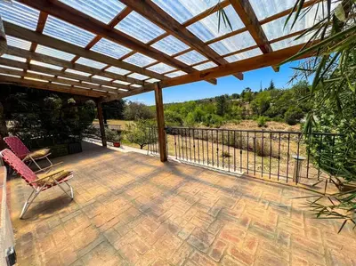 a patio with a wooden pergola and a chair at Hospedaje Frente al Rio el Rancho in Santa Rosa de Calamuchita