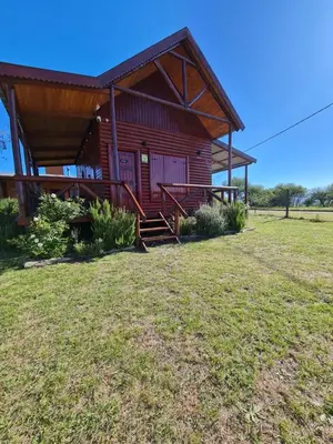 a log cabin with a grass yard in front of it at Cabañas en Los Reartes Córdoba in Villa General Belgrano