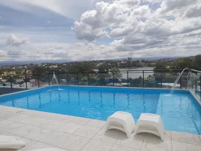 a swimming pool with two white chairs on a building at Dpto frente al Lago Carlos Paz in Villa Carlos Paz